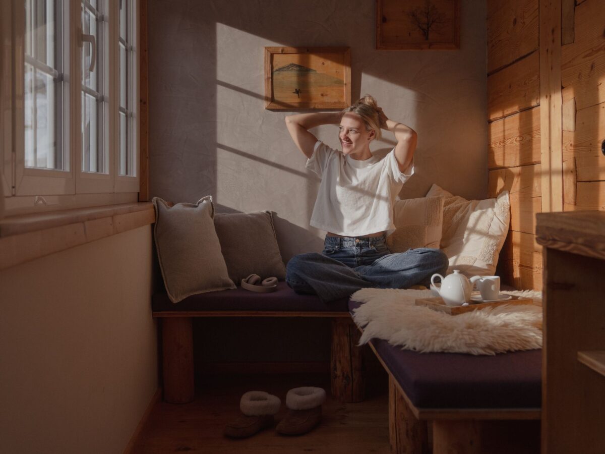 Gast entspannt am Morgen im Zimmer der Auenhütte im Kleinwalsertal mit Blick aus dem Fenster